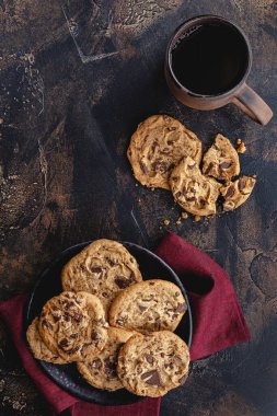 Bir tabak çikolata parçalı kurabiye ve bir fincan kahve kırsal bir ahşap masada. Genel Görünüm