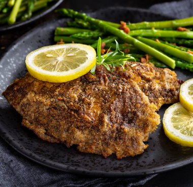 Limon dilimleri ve siyah tabakta kuşkonmazlı fırında pişirilmiş tilapia balık filetosu.