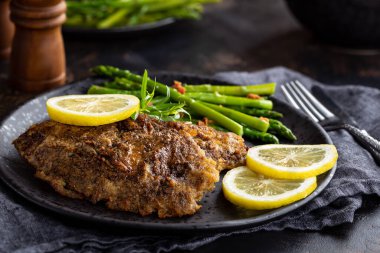 Limon dilimleri ve siyah tabakta kuşkonmaz ile pişirilmiş tilapia balığı filetosu.