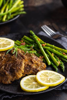 Limon dilimleri ve siyah tabakta kuşkonmaz ile pişirilmiş tilapia balığı filetosu.