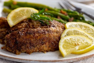 Yemek tabağında dilimlenmiş limon ve kuşkonmaz ile fırında pişirilmiş tilapia balık filetosu.
