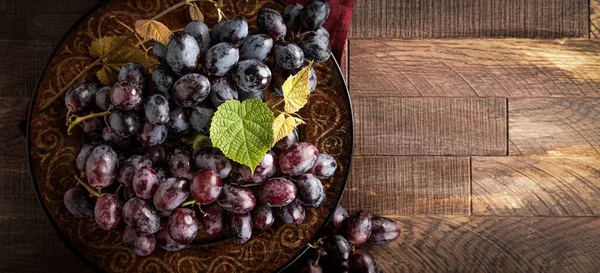 Kırsal ahşap bir arka planda, tabakta mor üzümler. Kopyalama alanı ile genel görünüm