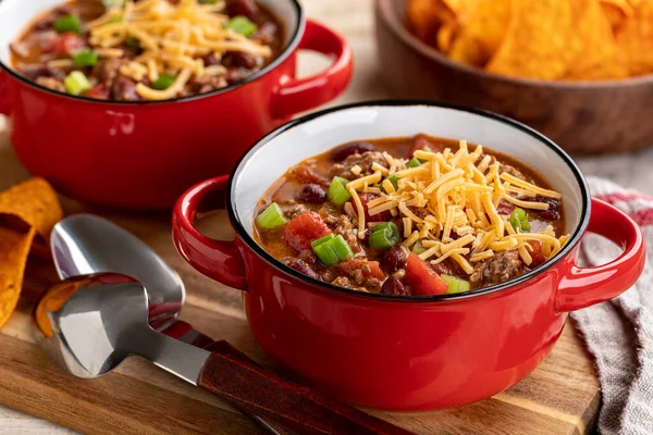 Bowl of chili con carne with shredded cheddar cheese on a wooden board