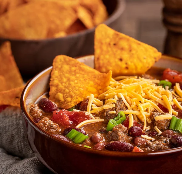 Closeup of bowl of chili con carne with cheddar cheese and nacho chips