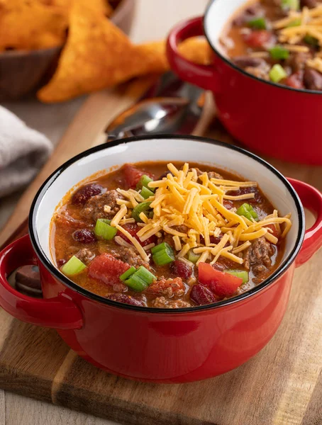 Bowl of chili con carne with shredded ceddar cheese on a wooden board