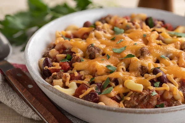 Closeup of bowl of chili macaroni with melted cheddar cheese on a wooden table