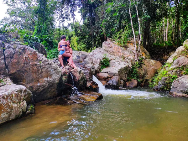 Samui, Tayland - 21.09.2018: Balayı. Aşık yeni evliler küçük bir şelalenin yanındaki bir taşın üzerinde oturun..