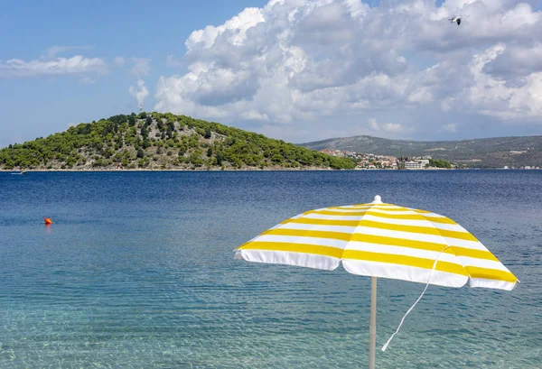 White and yellow sun umbrella on coast od Adriatic sea. Summer holiday in Croatia.