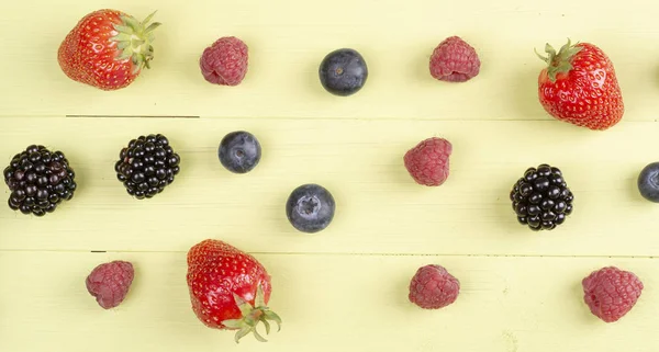 Soft fruits like strawberry, raspberry, blackberry on a green wooden table. Top view