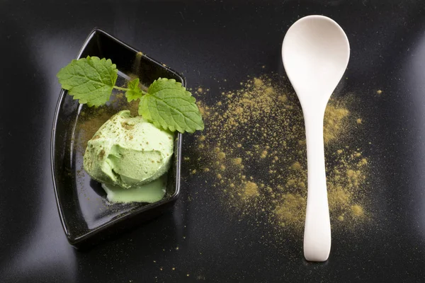 Green tea ice cream in a bowl with a teaspoon on a black plate. Top view
