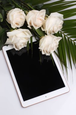 Beyaz bir yüzey üzerinde yatan beyaz güller ve yapraklar. boş ekranlı tablet. Soluk şeftali arka planda üst görünümü kadar stilde mock.