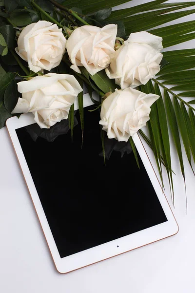 Beyaz bir yüzey üzerinde yatan beyaz güller ve yapraklar. boş ekranlı tablet. Soluk şeftali arka planda üst görünümü kadar stilde mock.
