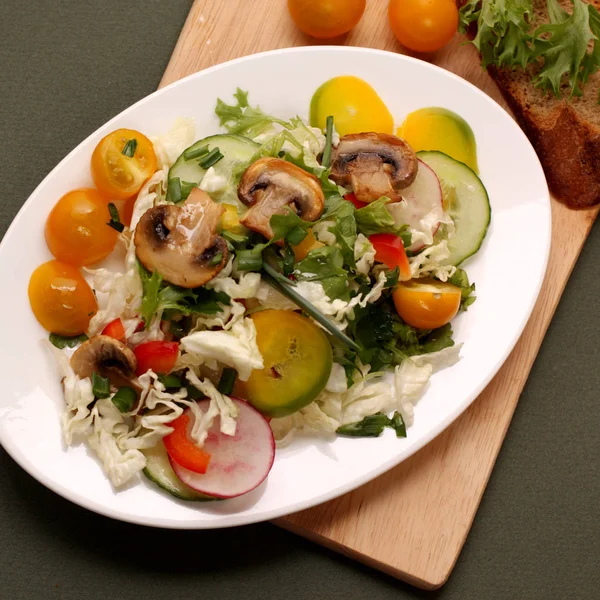 Tallrik med sallad med grönsaker, örter och champinjoner på ett träbord — Stockfoto