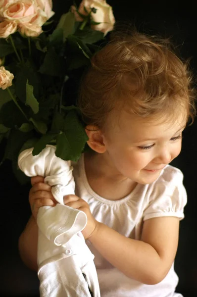 Malé děťátko s bílými růží v dlaních. Děvče v bílém tričku sedí na černém pozadí. — Stock fotografie