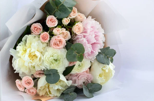 Beautiful delicate bouquet of mixed flowers on a light background. Flower background. Flower shop concept, flower delivery. Close-up of a bouquet of peonies and roses.