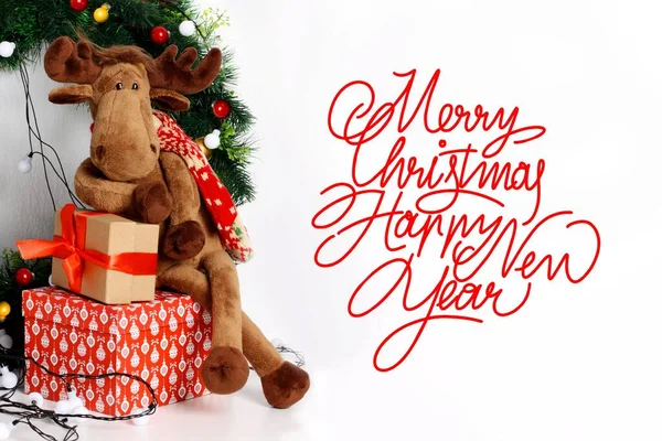Christmas card. Merry Christmas and Happy New Year. Text with a toy Christmas deer and gifts on a white background.