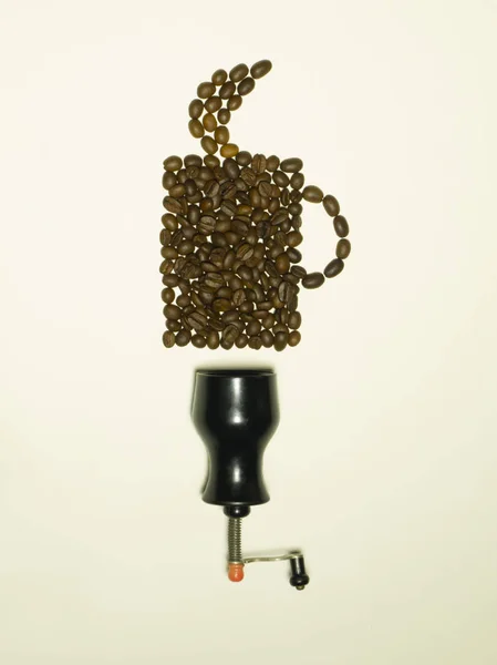 Coffee grinder and beans of aromatic coffee laid out in the form of a mug. Top view. Coffee grinder with roasted coffee beans. Coffee beans and grinder on light background.
