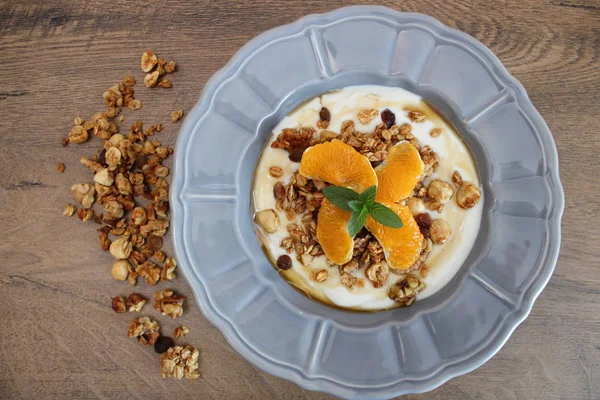 Granola bowl with soy yogurt and orange slices on a wooden table, grey plate