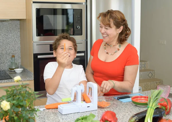 Η μητέρα και ο γιος ετοιμάζουν το γεύμα στην κουζίνα ευτυχισμένοι. Αστειεύεται και γελάει με ένα κομμάτι καρότο — Φωτογραφία Αρχείου