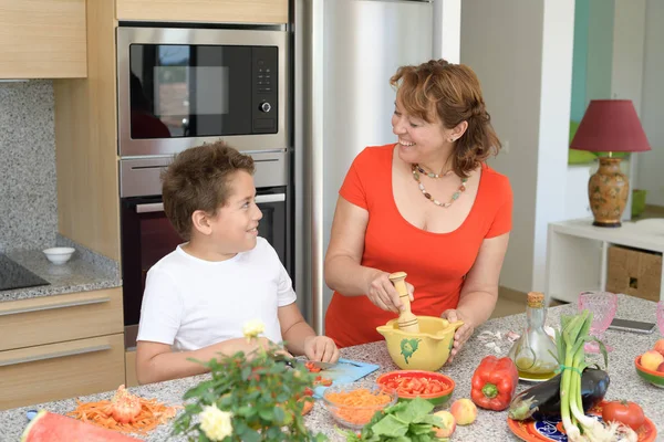 Madre e hijo preparando el almuerzo y sonríe. Hijo corta pimiento rojo — Foto de Stock