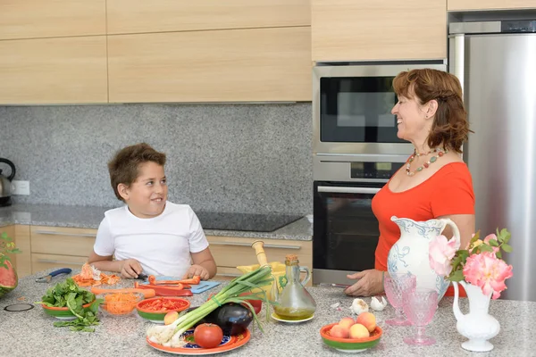 Η μητέρα και ο γιος ετοιμάζουν μεσημεριανό και χαμόγελα. Ο γιος κόβει το κόκκινο πιπέρι — Φωτογραφία Αρχείου