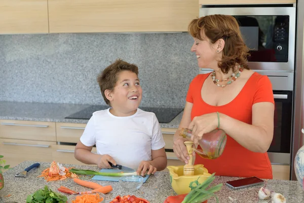 Madre e hijo preparando el almuerzo y sonríe. Hijo corta ajo — Foto de Stock