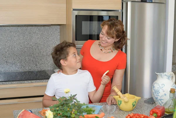 Anya és fia készít ebédet és mosolyt. Gyermek ad fokhagymát az anyja — Stock Fotó