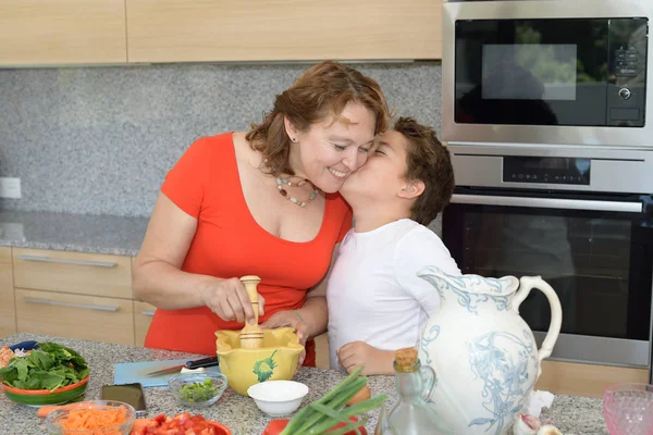Fia megcsókolja az anyját, miközben elkészíti az ebédet — Stock Fotó
