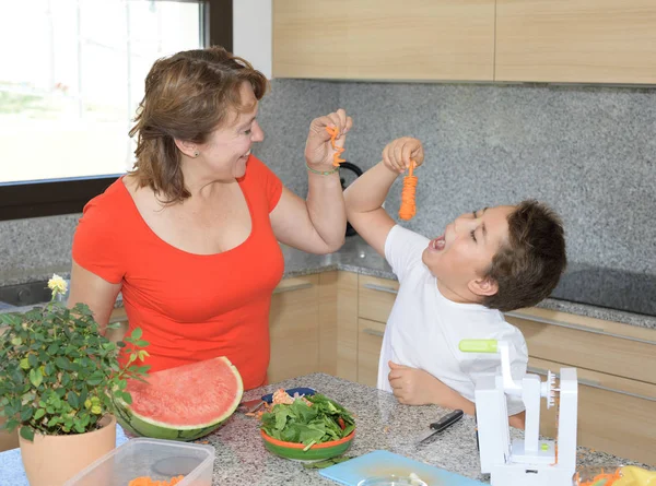 Η μητέρα και ο γιος ετοιμάζουν μεσημεριανό και χαμόγελα. Κάνουν πλάκα με ένα σκαλιστό καρότο — Φωτογραφία Αρχείου