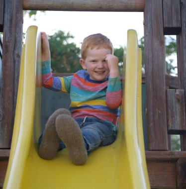 5 yaşındaki kızıl saçlı mutlu çocuk bir slayt oturur ve gülümseyerek