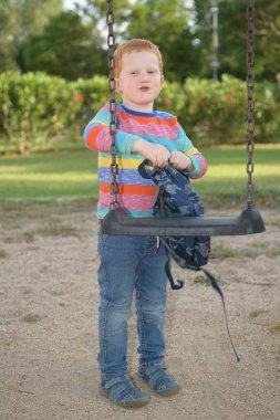 Okula gitmeden önce sırt çantasını salıncakta gören 5 yaşındaki kızıl saçlı mutlu çocuk