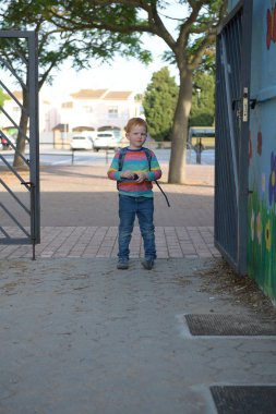 5 yaşında kızıl saçlı çocuk okulun önünde duruyor. Biraz üzgün.