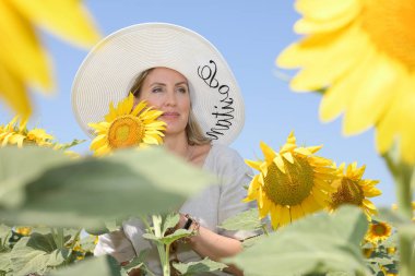 Şapkası olan genç kadın ayçiçeği tarlasında gülümsüyor ve hayal kuruyor. Aşağıdan görüntüle