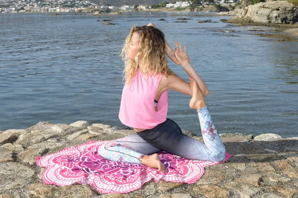 Молода дівчина робить йогу на невеликій пляжній пристані з середземноморським прибережним містом у фоновому режимі. Залишатися в формі. ЕКА пада Rajakapotoаa варіант йоги пози — стокове фото