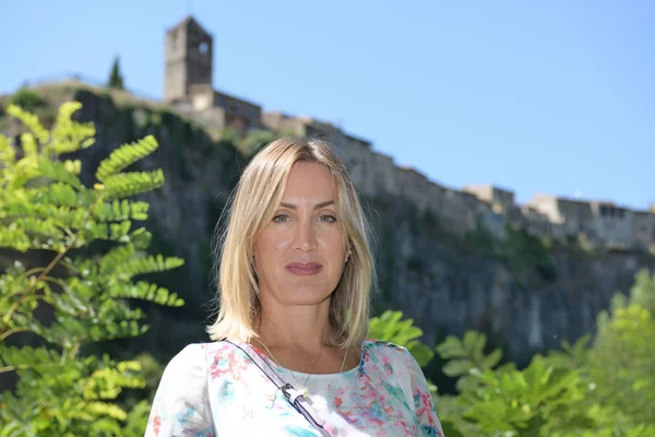 Donna bionda che guarda la macchina fotografica in un ambiente naturale con un villaggio medievale sullo sfondo chiamato Castellfollit de la Roca in Catalogna — Foto Stock