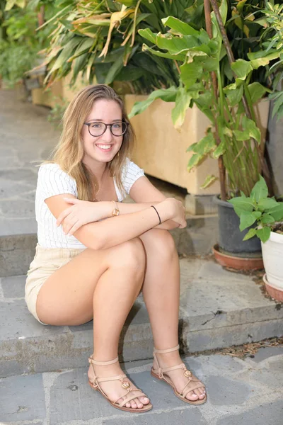 戴着眼镜的金发女孩坐在一个中世纪村庄的楼梯上 — 图库照片