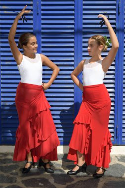 Flamenko dansı iki kız dikey portre. Tipik mendille simetrik bir pozisyondalar, mavi bir arka planda birbirlerine bakıyorlar.