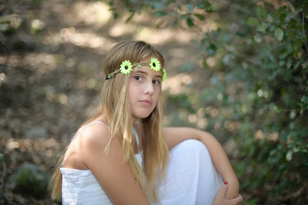 Menina sentada em uma floresta com uma coroa com flores — Fotografia de Stock