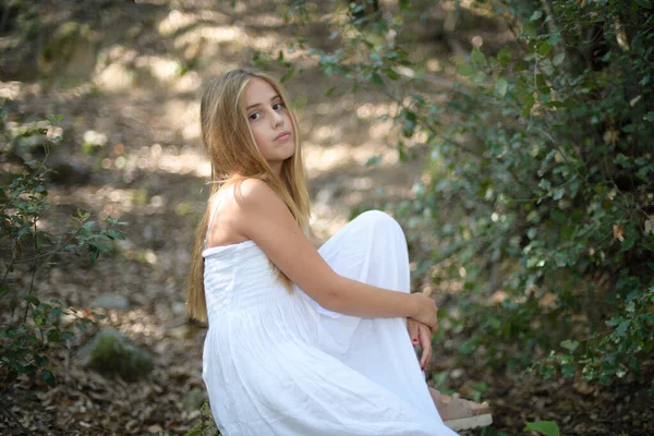 Chica sentada en un bosque en un vestido blanco mirando a la cámara — Foto de Stock