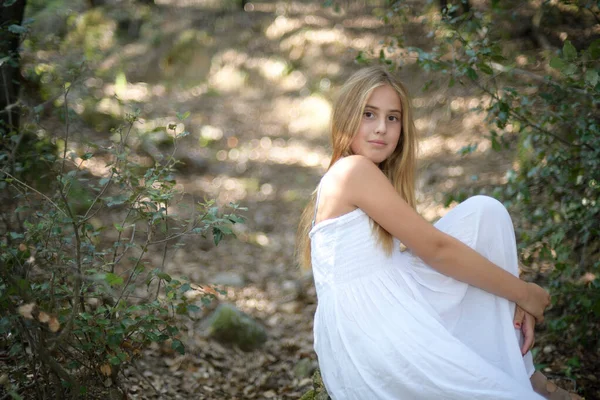 하얀 드레스를 입고 숲 속에 앉아 복제품 공간으로 카메라를 보고 있는 소녀 — 스톡 사진