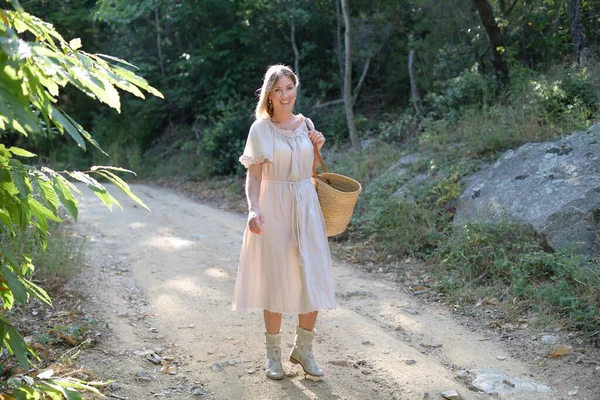 Gelukkige vrouw loopt langs een pad in een bos met een tas en kijkt naar de camera — Stockfoto