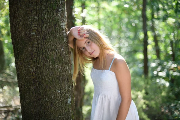 하얀 드레스를 입은 채 숲 속에서 나무에 기대고 있는 소녀 — 스톡 사진