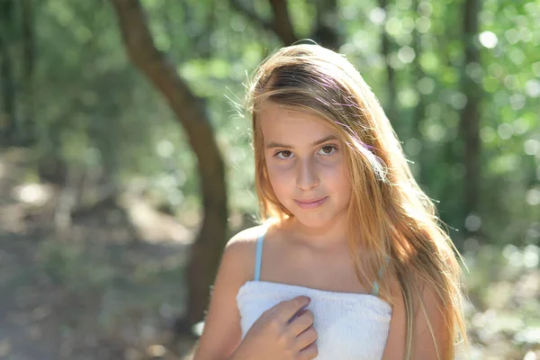 Retrato de una niña de pie en un bosque con un vestido blanco mirando — Foto de Stock