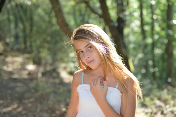 Retrato de una niña de pie en un bosque con un vestido blanco mirando — Foto de Stock