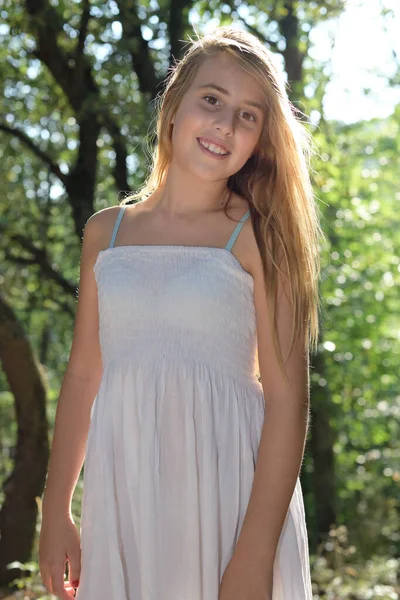 Retrato de uma menina de pé em uma floresta em um vestido branco olhando — Fotografia de Stock