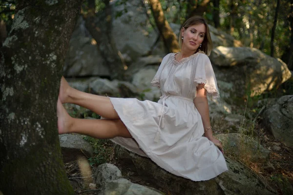숲 속에 앉아서 나무에 기대어 다리를 풀고 있는 여자 — 스톡 사진