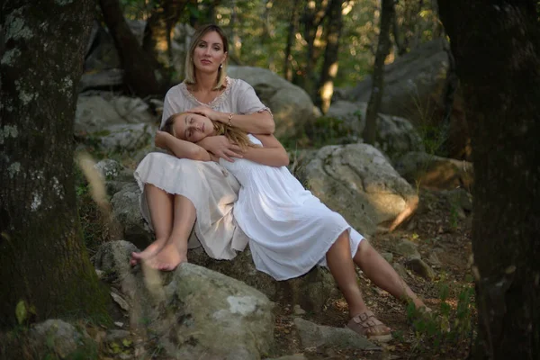 Ormanda oturan ve gün batımında kızı bacaklarının üzerinde uzanan bir kadın. — Stok fotoğraf