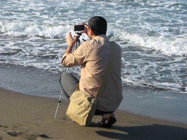 Fotoğraf çeken adam fotoğraf plajçekiyor. İran'daki Hazar sahilinde bir fotoğrafçı. Turist adam kamera tripod onun akıllı telefon ile bir deniz fotoğrafı çekiyor. 