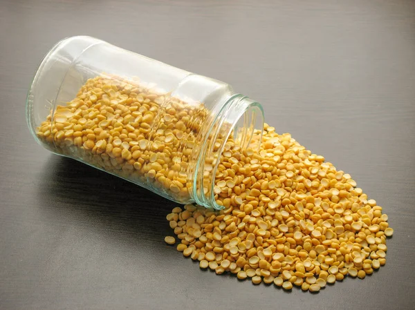 Yellow split dried peas  are poured from a glass jar on brown wooden surface.Yellow split dried peas in a glass jar on the wooden table.Yellow split dried peas in a glass dish. Wooden backgroun