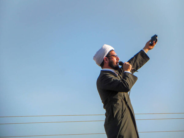 Karbala, Bagdad, Iraq, 06 09 2019: Speech by a Shia Muslim preacher. Шиитский клирик в специальной одежде с голубым небом
.